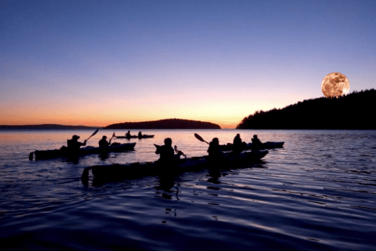 Kayakers at sunset with a large moon rising above the horizon